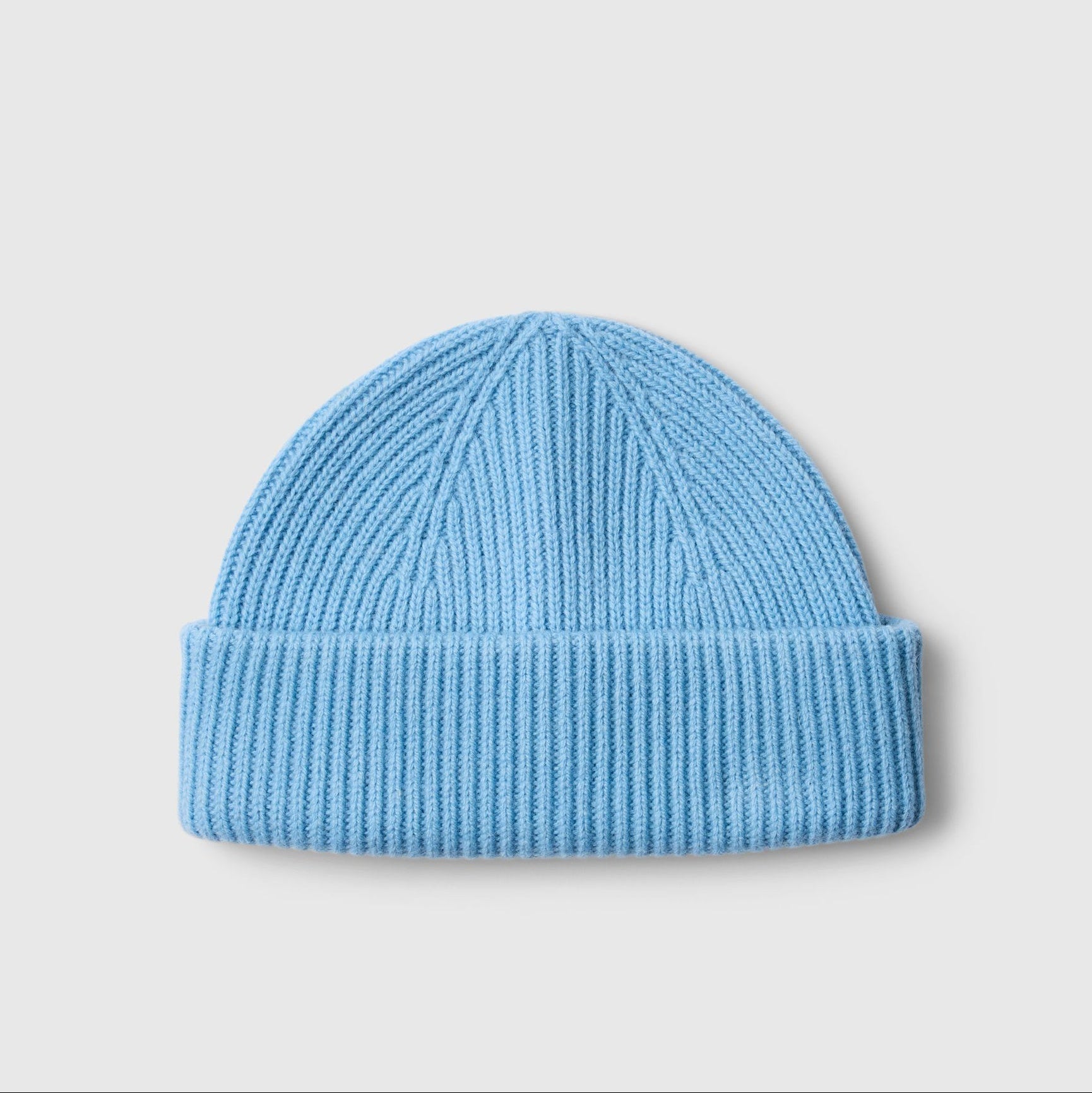 A light blue ribbed knit beanie hat, photographed flat against a neutral light gray background.