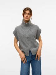 Woman wearing a gray knit vest and blue jeans on a white background
