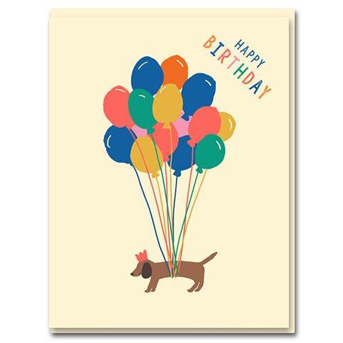 sausage dog is levitated by colourful balloons. 'happy birthday' written on the top corner. base baby pink