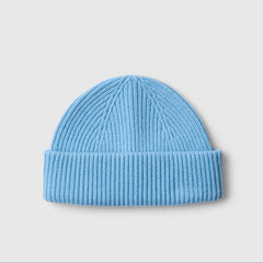A light blue ribbed knit beanie hat, photographed flat against a neutral light gray background.