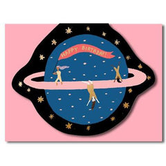 3 people jumping around the planet Saturn. One of them carrying "happy birthday" written flag. base baby pink